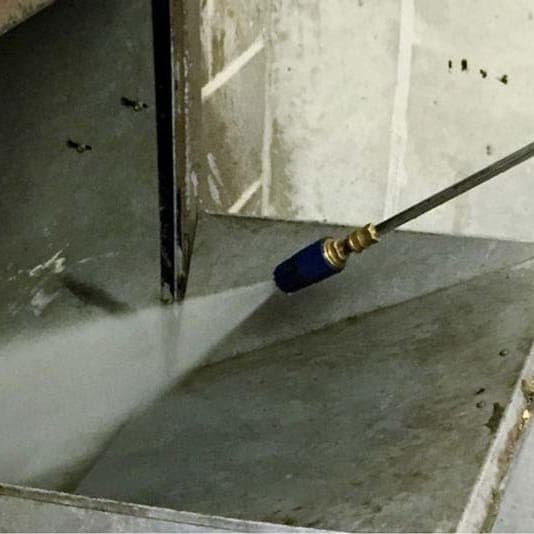 A pressure washer lance spraying hot water down into an open trash chute