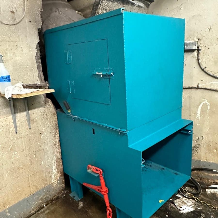 A teal painted trash compactor standing in a building trash room