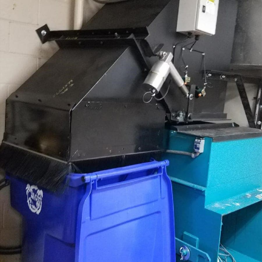 A sorter above a blue recycling toter and a compactor, in a trash room