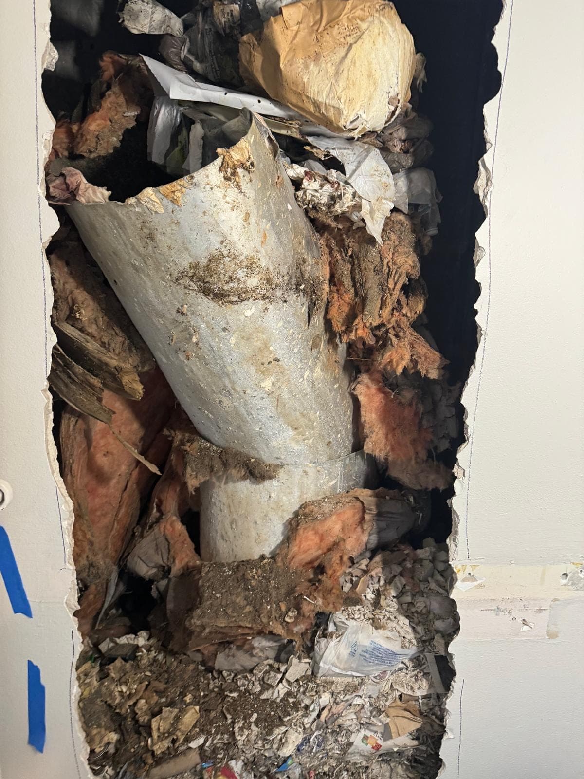 A failed trash chute inside a wall broken open around it