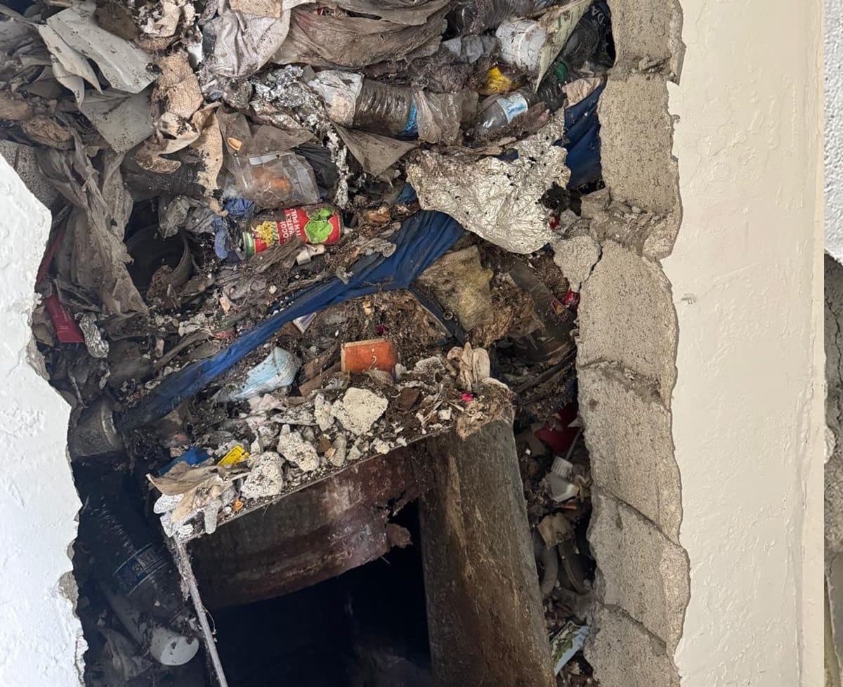 A chute packed solid with rubbish behind a broken wall